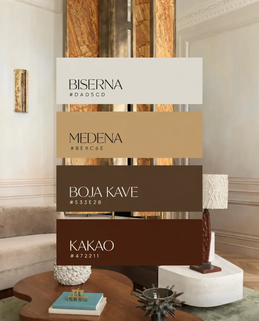 DETALJAN OPIS: Pozadinska fotografija prikazuje elegantno uređen dnevni boravak u klasičnom, svijetlom stilu. U gornjem dijelu slike dominira arhitektonski element — tanak vertikalni stup ili pregrada obložena mramorom u toplim nijansama smeđe, narančaste i boje meda, s vidljivim prirodnim žilicama kamena, uokviren tankim metalnim (mjedenim ili brončanim) rubovima koji se spuštaju od vrha do dna kadra. Zidovi s obje strane su bijeli, s klasičnim profiliranim lajsnama i ukrasnim štukaturama pri stropu. Lijevo na zidu nalazi se uska vertikalna zidna svjetiljka u mjedenom/zlatnom tonu, s teksturiranom površinom nalik drvetu ili kamenu. U donjem dijelu fotografije vidljiv je dio interijera: lijevo je bež tapecirana sofa s mekim jastucima, djelomično izvan kadra. U sredini se nalazi okrugli drveni stol nepravilnog, organskog oblika, na kojem stoje: bijela keramička vaza teksturirane površine nalik ananasu, dvije knjige (gornja s plavim koricama) s malim zlatnim ukrasnim predmetom (nalik minijaturnoj stolici ili skulpturi) na vrhu, te tamna metalna/keramička posuda nepravilnog, bodljikavog oblika nalik morskom ježu ili koraljnom grmu. Pod je od drvenog parketa položenog u riblju kost, djelomično prekriven svijetlozelenim/sivim tepihom. Desno od stola nalazi se stolna svjetiljka s tamnim rezbarenim drvenim postoljem i bež tekstiliziranim sjenilom s geometrijskim uzorkom, postavljena na bijeli kameni/betonski podest nepravilnog, zaobljenog oblika. Preko ove pozadinske fotografije, u sredini kompozicije, okomito su poslagane četiri pravokutne trake boja koje predstavljaju paletu boja, svaka s nazivom i HEX kodom: Prva traka, pri vrhu, svijetle krem/bjelkaste boje, nosi naziv "BISERNA" ispisan velikim tamnim slovima, a ispod naziva manjim slovima kod "#DAD5CD". Druga traka je toplo zlatno-smeđa, boje meda, s nazivom "MEDENA" ispisanim tamnim slovima i kodom "#BE9C6E" ispod. Treća traka je tamna, zemljano-smeđa nijansa, s nazivom "BOJA KAVE" ispisanim svijetlim (bijelim/krem) slovima i kodom "#533E2B" ispod. Četvrta, donja traka, najtamnija je i ima crveno-smeđi, čokoladni ton, s nazivom "KAKAO" ispisanim svijetlim slovima i kodom "#472211" ispod. Sve četiri trake su poravnate po širini i poslagane jedna ispod druge, formirajući okomiti niz preko središnjeg dijela fotografije, dok rubovi fotografije (lijevo i desno) ostaju vidljivi oko traka.